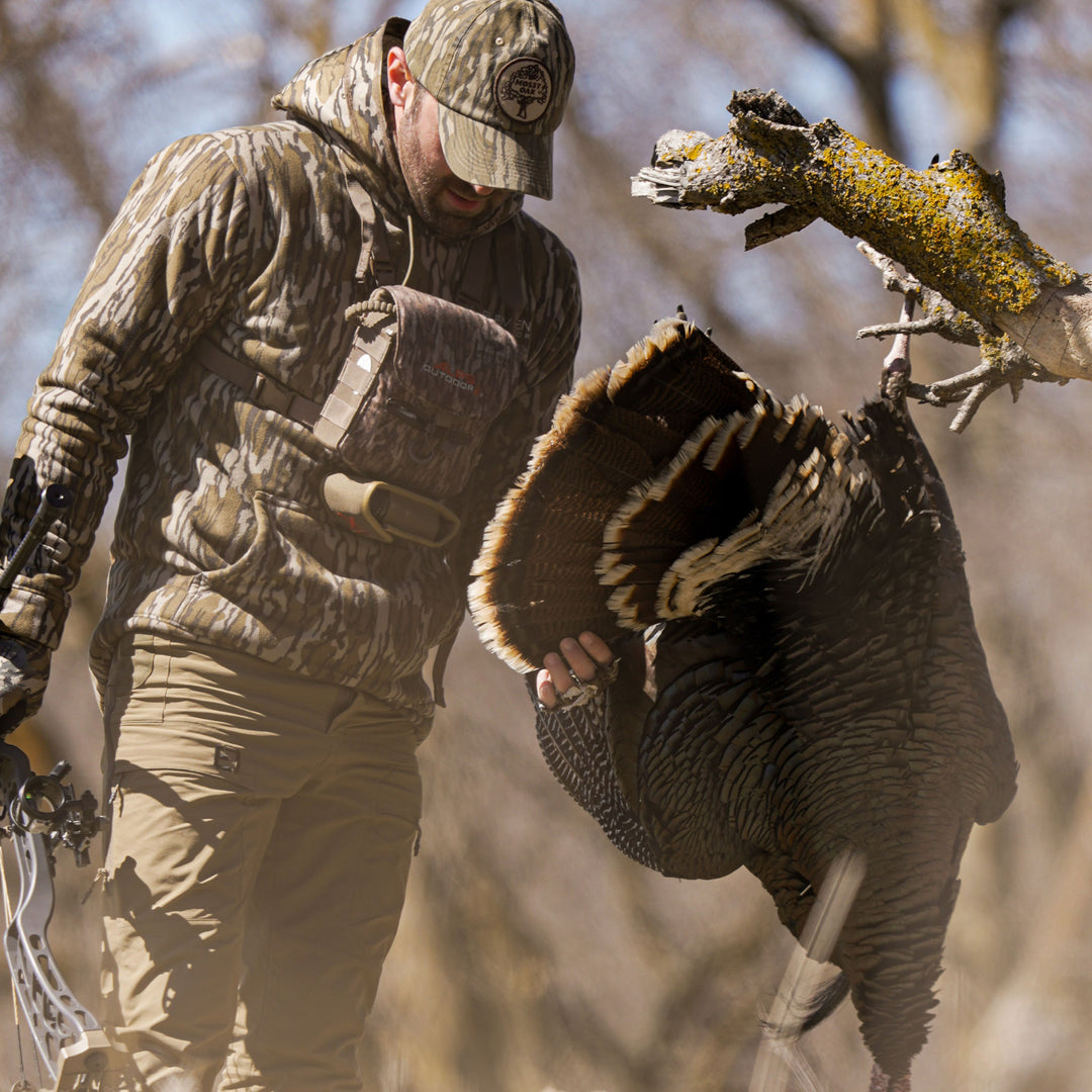 Turkey Hunter admiring a turkey after a hunt wearing a mountaineer hoodie#color_original-bottomland