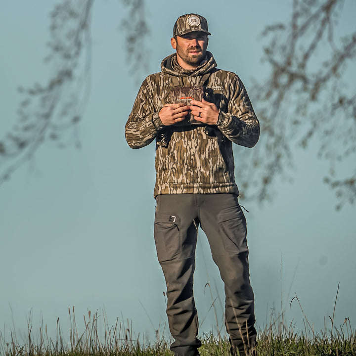 Man standing in a field wearing a mountaineer hoodie#color_original-bottomland