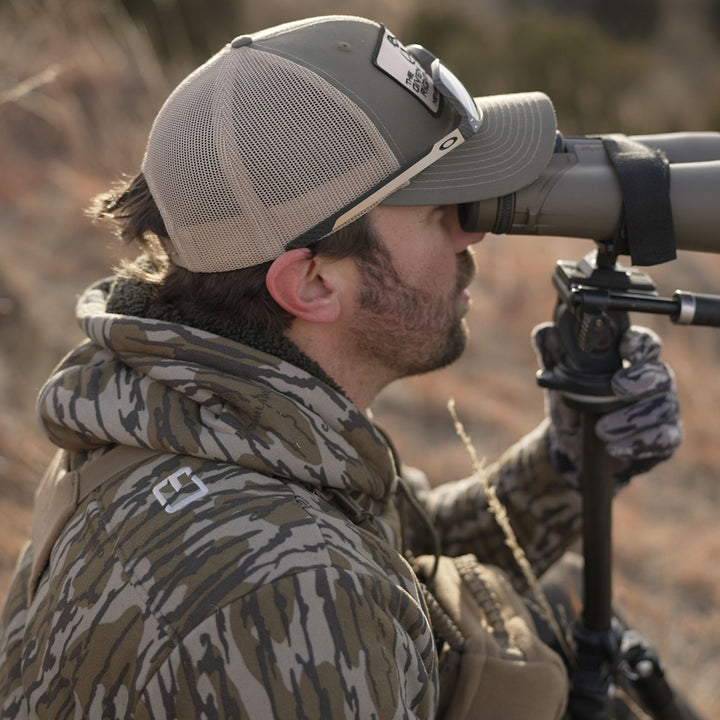 Man looking through binoculars wearing Mountaineer Hoodie#color_original-bottomland